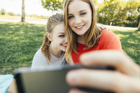 Zwei glückliche Teenager-Mädchen machen ein Selfie auf einer Wiese, lizenzfreies Stockfoto