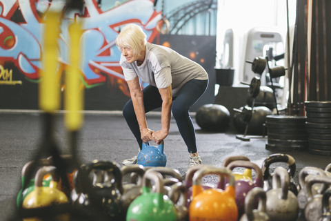 Senior woman in gym lifting kettlebell stock photo