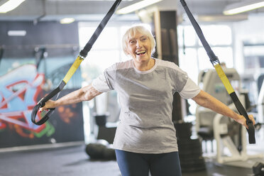 Glückliche ältere Frau im Fitnessstudio beim Suspensionstraining - MADF000518