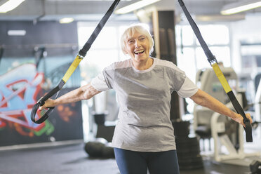 Happy senior woman in gym doing suspension training - MADF000518