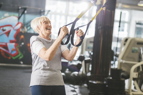 Glückliche ältere Frau im Fitnessstudio beim Suspensionstraining, lizenzfreies Stockfoto