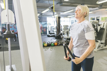 Smiling senior woman in gym exercising at cable machine - MADF000520