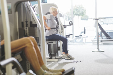 Ältere Frau im Fitnessstudio, die an einer Dip-Maschine trainiert - MADF000523