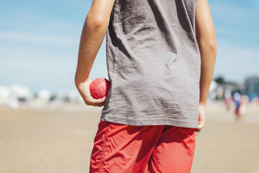 Back view of boy standing on the beach holding red boccia bowl in his hand - GEMF000316