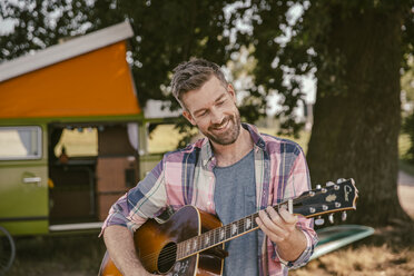 Lächelnder Mann vor einem Lieferwagen spielt Gitarre - MFF002005