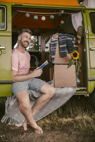 Lächelnder Mann liest ein Buch im Van, lizenzfreies Stockfoto