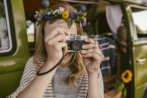 Hippie-Frau, die mit einer analogen Kamera vor einem Lieferwagen fotografiert, lizenzfreies Stockfoto