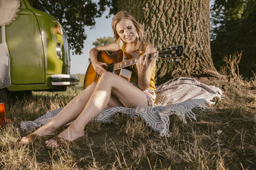 Junge Frau spielt Gitarre an einem Baum neben einem Lieferwagen - MFF002043