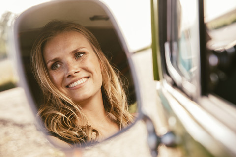 Gesicht einer lächelnden Frau spiegelt sich im Außenspiegel eines Lieferwagens, lizenzfreies Stockfoto