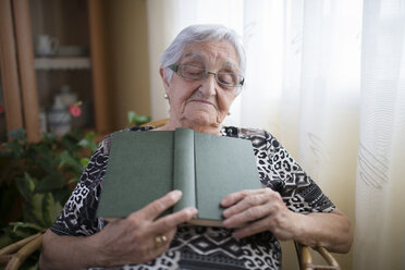 Senior woman having a nap with book in her hands at home - RAEF000316