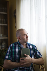 Pensive man with book at home - RAEF000327