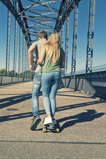 Rückenansicht eines jungen verliebten Paares auf einem Skateboard - MEMF000938