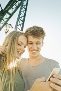 Lächelndes junges Paar schaut gemeinsam auf ein Smartphone - MEMF000940