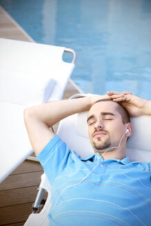 Entspannter junger Mann am Pool und beim Musikhören - TOYF001061