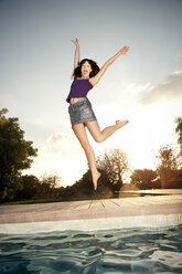 Exuberant young woman jumping at the poolside - TOYF001083