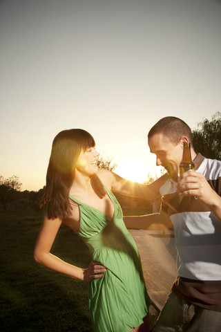 Glückliches junges Paar tanzt mit Bierflasche bei Sonnenuntergang, lizenzfreies Stockfoto