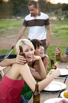 Happy friends embracing at garden table on a barbecue with beer bottles - TOYF001218