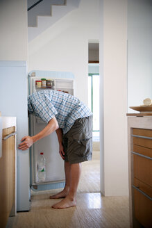 Young man standing in the kitchen searching something in the fridge - TOYF001106