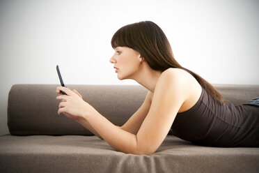 Young woman lying on a couch looking at her smartphone - TOYF001112