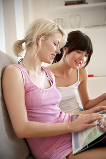 Two young women reading magazine together - TOYF001128