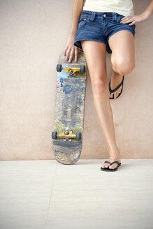 Legs of young woman with longboard in front of a wall - TOYF001137