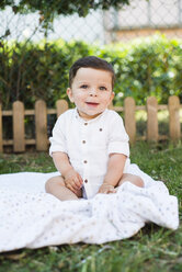 Porträt eines lächelnden kleinen Jungen, der auf einer Decke im Garten sitzt - RAEF000333