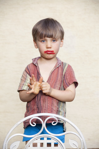 Porträt eines kleinen Jungen mit rotem Lippenstift auf seinem Gesicht und schmollendem Mund, lizenzfreies Stockfoto