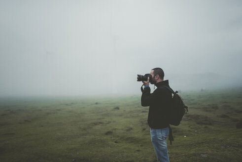Spain, Ortigueira, photographer taking pictures on a meadow with fog - RAEF000342