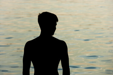 Silhouette eines Teenagers vor einem See in der Dämmerung - TCF004839