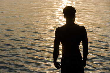 Silhouette of teenage boy in front of a lake at backlight - TCF004840