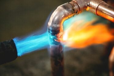 Ein Klempner-Heißgaslötbrenner erhitzt ein Kupfer-Winkelstück zum Verbinden zweier Kupfer-Wasserrohre - EHF000203