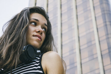 Porträt eines Teenagers mit Kopfhörern vor einem Wolkenkratzer - ABZF000106
