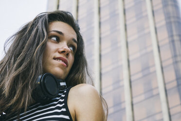 Portrait of teenage girl with headphones in front of skyscraper - ABZF000106