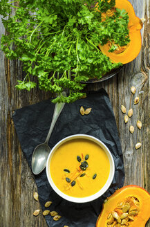 Selbstgemachte Kürbissuppe mit Kürbiskernen und Petersilie auf einem Holztisch - ODF001219