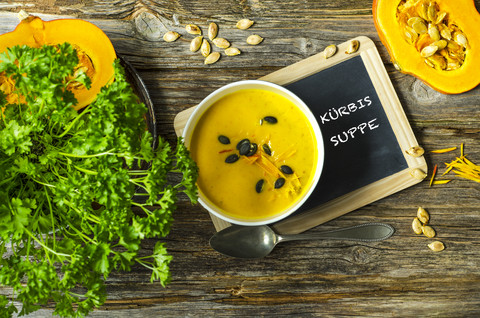 Selbstgemachte Kürbissuppe mit Kürbiskernen, Petersilie und einer Schiefertafel auf einem Holztisch, lizenzfreies Stockfoto