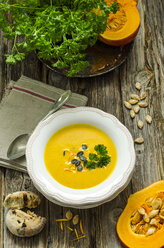 Selbstgemachte Kürbissuppe mit Kürbiskernen, Petersilie und einem Brötchen mit Oliven und Tomaten auf einem Holztisch - ODF001222