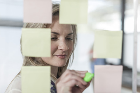 Frau im Büro schreibt auf Klebezettel, lizenzfreies Stockfoto