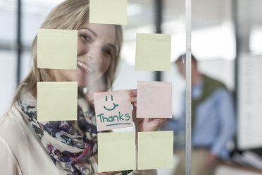 Woman in office writing thanks on sticky note - ZEF007416