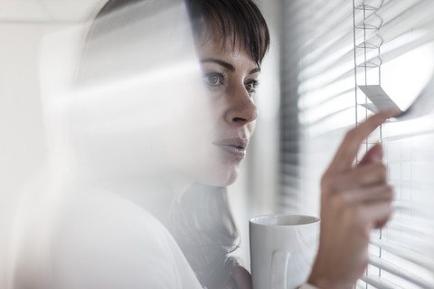 Frau im Büro schaut durch Jalousien, lizenzfreies Stockfoto