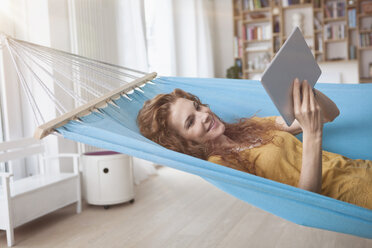 Smiling woman at home lying in hammock using digital tablet - RBF003052