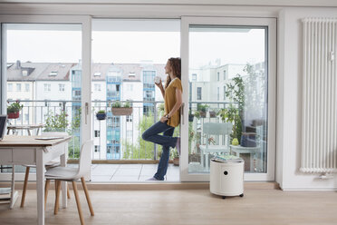 Woman with cup of coffee leaning against balcony door - RBF003124