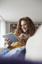 Lächelnde Frau zu Hause auf der Couch sitzend mit digitalem Tablet - RBF003076