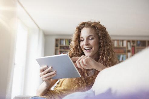 Lächelnde Frau zu Hause auf der Couch sitzend mit digitalem Tablet - RBF003077