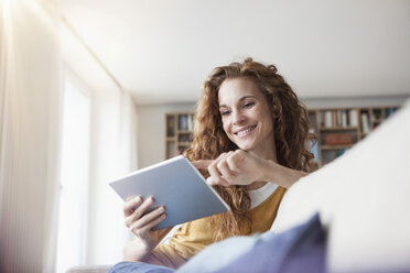 Smiling woman at home sitting on couch using digital tablet - RBF003078