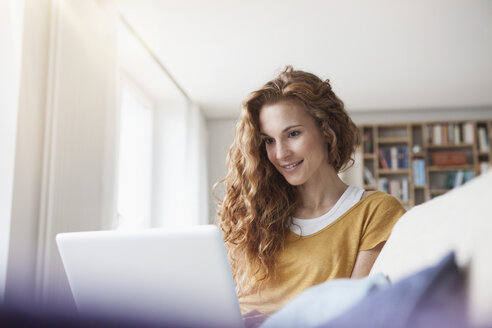 Frau zu Hause auf der Couch sitzend mit Laptop - RBF003079