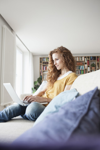 Frau zu Hause auf der Couch sitzend mit Laptop, lizenzfreies Stockfoto