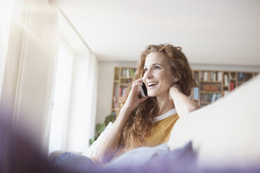 Lächelnde Frau zu Hause auf der Couch sitzend und mit dem Handy telefonierend - RBF003083