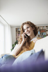 Smiling woman at home sitting on couch talking on cell phone - RBF003129