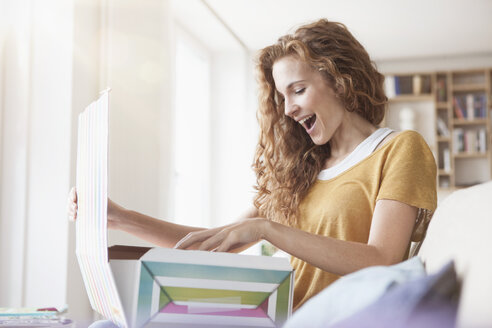 Happy woman at home sitting on couch unpacking parcel - RBF003084