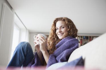 Smiling woman at home sitting on couch holding cup - RBF003090